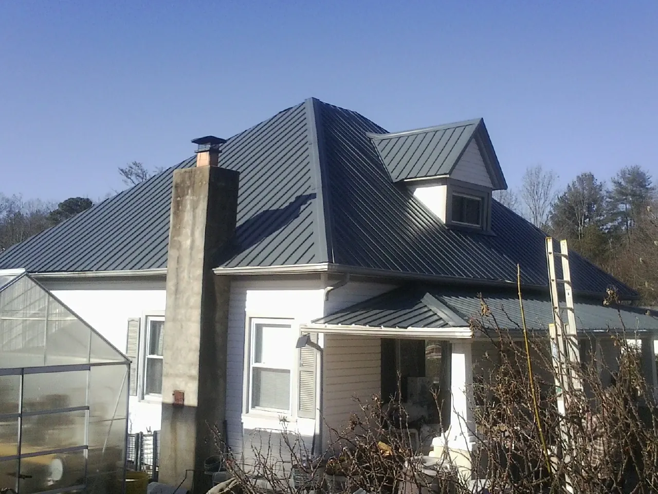 Dark blue standing seam metal roof on a white farmhouse with dormer — Slate & Tile Roof Repair by Roofing Brothers in Irene