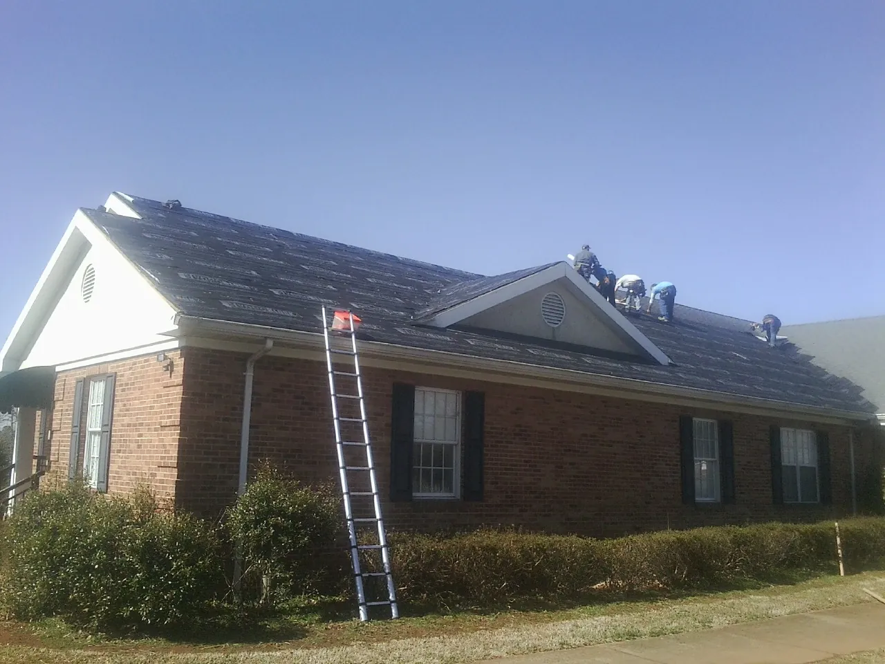 Crew tearing shingles off a brick ranch roof with a ladder set — Emergency Roof Repair work by our crew in Irene