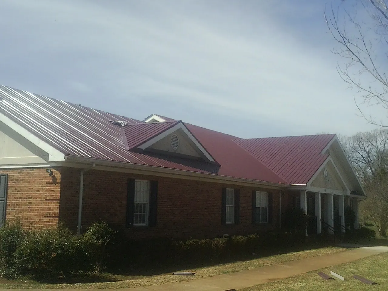 Red metal roof with gabled entries on a long brick building, from a Hail Damage Roof Repair job in Irene
