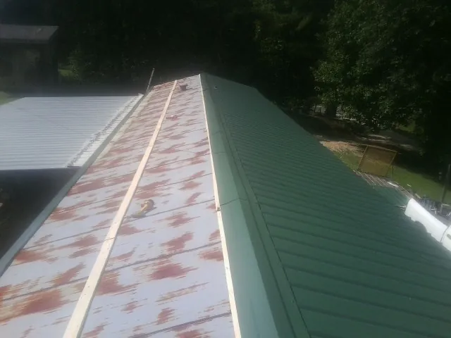 Old rusted panels beside newly installed green metal roofing — Wind Damage Roof Repair by Roofing Brothers in Irene