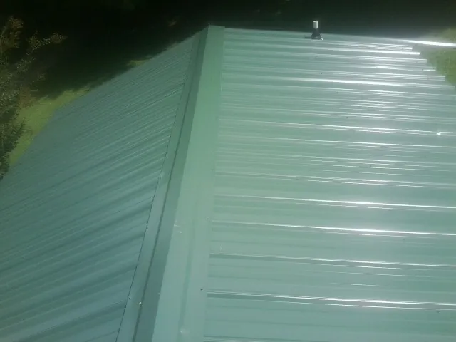 New green metal panels meeting at the ridge of a roof — Flat Roof Repair work by our crew in Irene
