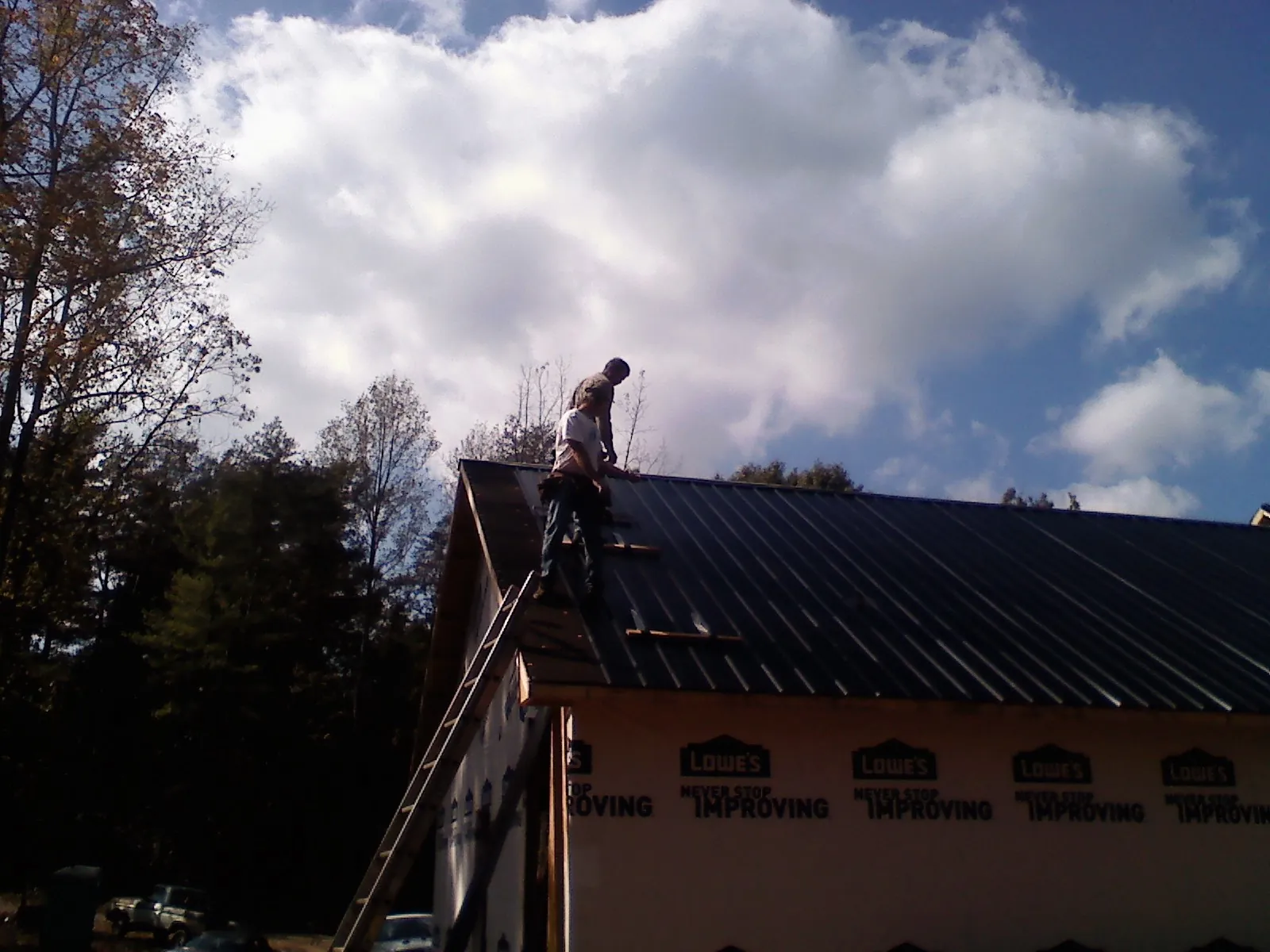 Roofer fastening dark metal panels high against a cloudy sky, from a Roof Inspection job in Irene