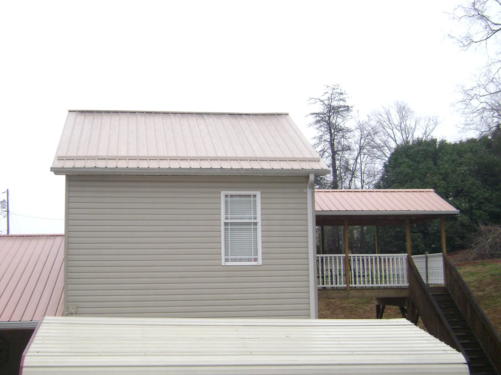Tan metal roofs on a two story addition and attached porch, from a Roof Replacement job in Irene